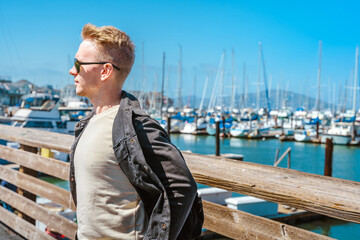 A young man stands on pier 39 leaning on a fence, San Francisco