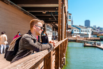 Fototapeta na wymiar A young man stands on pier 39 leaning on a fence, San Francisco