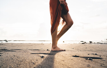 Unrecognizable slim female in light dress on sandy shore