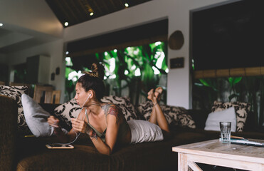 Tattooed woman listening to music lying on sofa in room