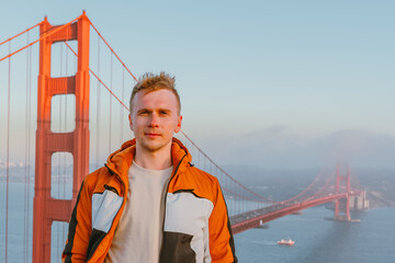 Young man on a hill overlooking the Golden Gate Bridge at sunset in San Francisco - obrazy, fototapety, plakaty