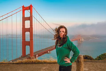 Foto auf Acrylglas Golden Gate Bridge A young woman in a green hoodie stands on a hill overlooking the Golden Gate Bridge during sunset, San Francisco