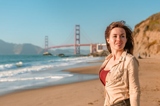 Beautiful young woman with long hair walks on the beach overlooking the Golden Gate Bridge in San Francisco