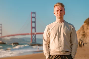Foto op Plexiglas Golden Gate Bridge A young man walks on the beach overlooking the Golden Gate Bridge in San Francisco, USA
