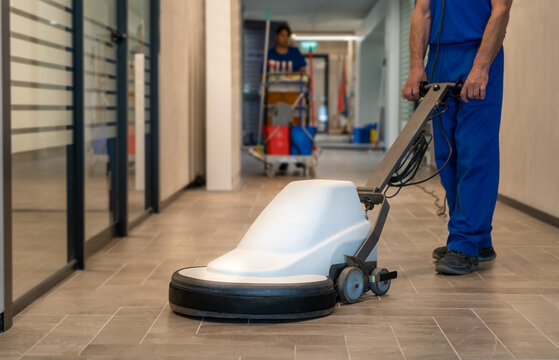 Professional cleaner polish hard floor with high speed machine.Cleaning leady with trolley is in the background