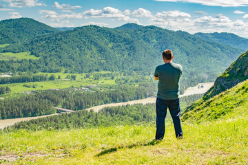 a man stands on the top of a mountain and looks thoughtfully at a mountain valley with a river