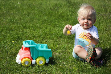 cute adorable little child playing with toy car lorry on the green grass in the park
