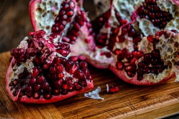 Sliced, peeled pomegranate fruit lies on a kitchen board on a wooden table.