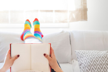 Lesbian woman relaxing at home on a sofa reading a book and dressed in rainbow colored socks. LGBT...