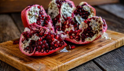 Sliced, peeled pomegranate fruit lies on a kitchen board on a wooden table.