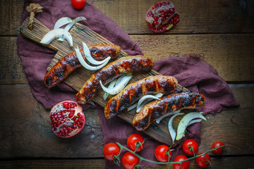 Traditional Caucasian meat sausages kupati served on wooden board with onion, tomatoes and pomegranate. Dark mood style. Top view of dish kupaty 
