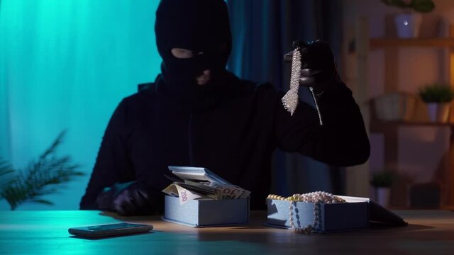 Portrait of a robber in a balaclava with jewelry in his hands