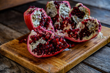 Sliced, peeled pomegranate fruit lies on a kitchen board on a wooden table.