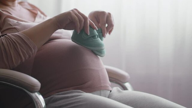 Happy pregnant woman expecting a baby. Pregnant woman feeling happy at home while taking care of her child. Pregnant woman resting alone at home strokes touches her big belly, close up. Slow motion