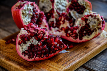 Sliced, peeled pomegranate fruit lies on a kitchen board on a wooden table.