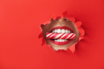 Naklejka premium Beautiful young woman with candy in mouth visible through hole in color paper