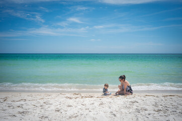 Mother and son enjoy white sand and blue turquoise water on a beach trip at bottom right corner of photo with negative space for type or text