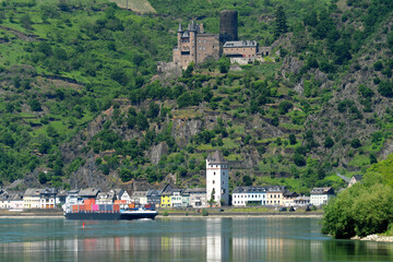 Fototapeta na wymiar Containerschiff auf dem Rhein im oberen Mittelrheintal und Panorama von St. Goarshausen mit Burg Katz - Stockfoto
