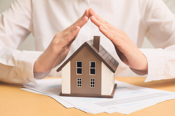 Woman with house model on color table, closeup. Property insurance concept