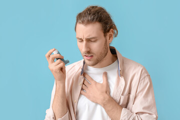 Young man with inhaler having asthma attack on color background
