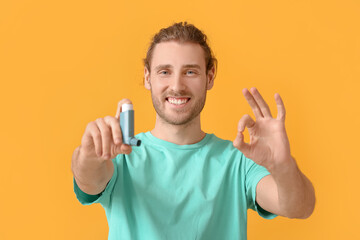 Young man with inhaler showing OK on color background