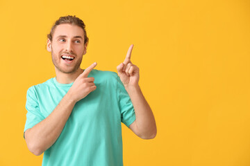 Handsome man pointing at something on color background