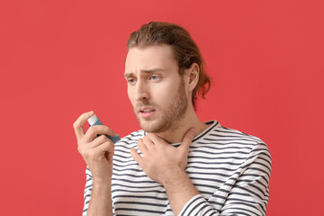 Young man with inhaler having asthma attack on color background