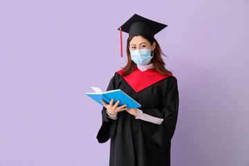 Female graduating student in protective mask and with book on color background