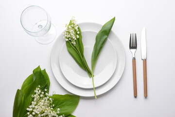 Beautiful table setting with lily-of-the-valley flowers on light background