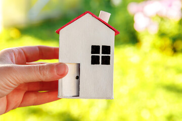 Obraz na płótnie Canvas Miniature model house in female woman hand on green outdoor background. Eco Village, abstract environmental background. Real estate mortgage property insurance dream home ecology concept.
