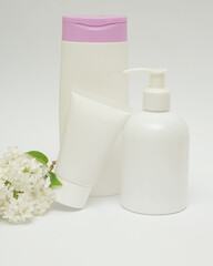 Fototapeta na wymiar Three bottles with a cosmetic product on a white background with lilac flowers. 