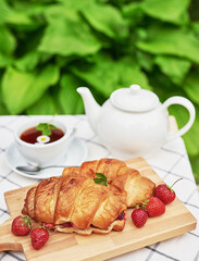 Breakfast outside. Cup of tea, strawberries, cherries, croissants on table. Summer picnic. Good morning concept.