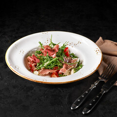 Salad with fresh herbs, cherry tomatoes, Mozzarella cheese and Parma ham on a black background.