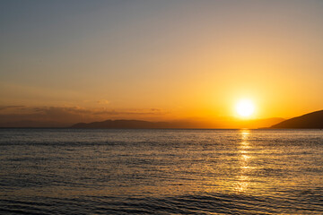Beautiful golden sunset over the lake. The summer sun goes down behind the mountains.