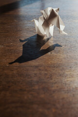 Origami elephant made of brown paper over wooden background.