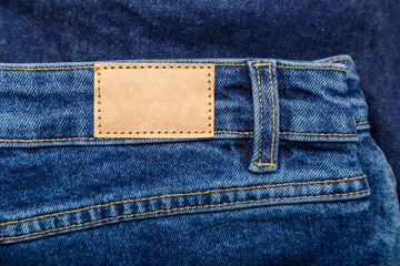 Brown blank label, leather tag on denim pants background. Blank mockup beige leather label. Blue...