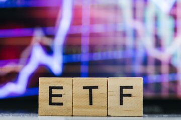 ETF Exchange-traded fund wooden letters and blurry stock market charts in the background 