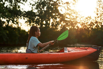 Side view of young woman looking relaxed while kayaking in a lake surrounded by nature on a late...