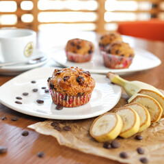 Fresh muffins with raisins and cup of coffee on sunny blurred background. Light breakfast or dessert. Soft focus.