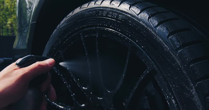 Employee works in car wash. Washing wheels with foam and water in auto service, close-up. Car detailing concept