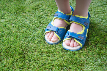 Tender kid legs in sandals close-up on the soft artificial grass