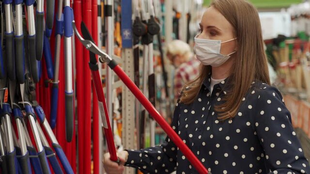 Woman in a medical mask chooses a pruner in a garden store