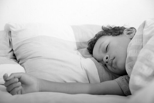 boy trying to sleep wrapped up in blanket in bed after having a good day stock photo
