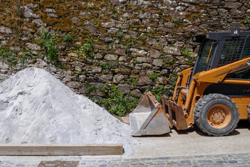 Yelllow backhoe with a pile of sand, cement, gravel