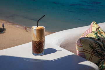 Glass of yummy iced coffee or greek freddo cappuccino on the seascape background on a summer sunny day at the Kythnos, Cyclades Islands, Greece.