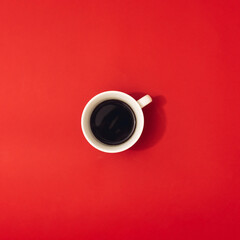 Striking cup of black coffee on red background. Minimal flat lay.