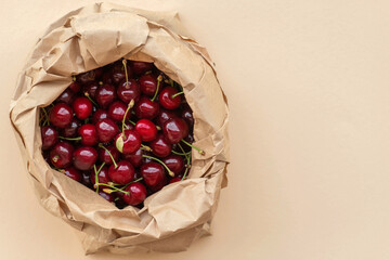 Ripe red cherries in an eco-friendly paper bag on a beige background.