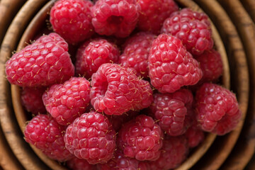 Ripe raspberries in a wooden container on a red background.