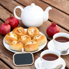Tea time. Blank area for message or greeting card. Appetizing cheesecakes or open pies with cottage cheese, two cups of tea on wooden table with pomegranates and teapot on it. Soft focus.