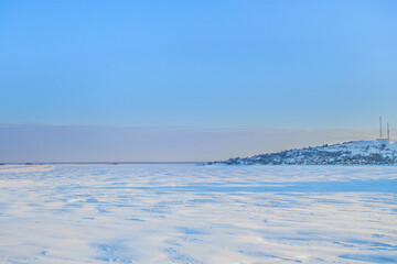 Fototapeta na wymiar Panorama of a wide frozen river in winter. On the right side you can see a coastal village or town. On the left, you can see the temporal road laid along the snowdrifts